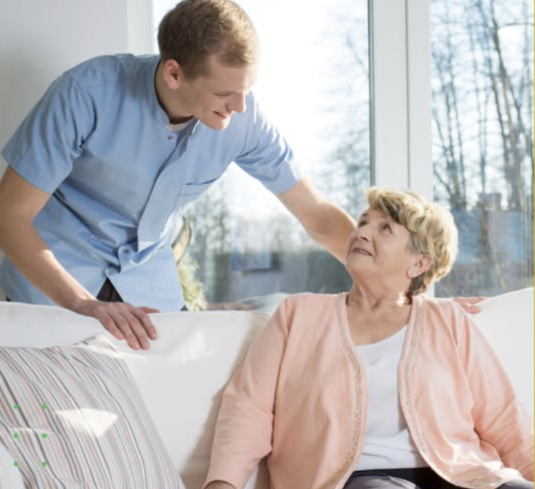 Caregiver assisting an elderly man with a warm smile, in a cozy living room filled with natural light in Cornelius, NC